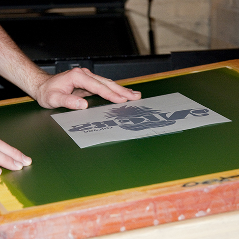 Before we can print, the image must be burned into the emulsion of the screen.  Here we are attaching the film to the screen, getting ready to be exposed.